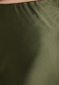 Olívazöld szövet sima textúrával, enyhe fényességgel és lágy ráncokkal, amelyek a puhaságot és a design folyékonyságát tükrözik.