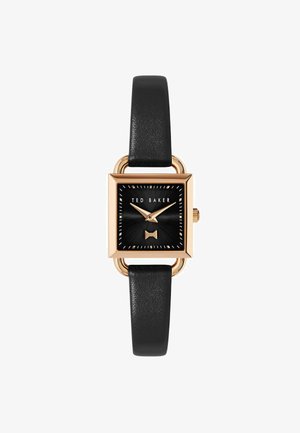 Négyzet alakú Ted Baker óra fekete számlappal, arany részletekkel és texturált masni díszítéssel. Fekete bőrszíjjal és arany tónusú fémrészekkel rendelkezik.