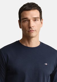 Marineblå langærmet t-shirt lavet af blødt bomuldsstof, med et lille logo på venstre brystområde og en klassisk rund hals.