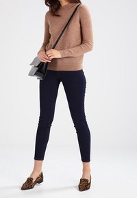 Brązowy sweter z dzianiny, ciemnoniebieskie tighty, czarna torba na ramię i brązowe mokasyny w lamparcie cętki, z okrągłym dekoltem i dopasowanym krojem.