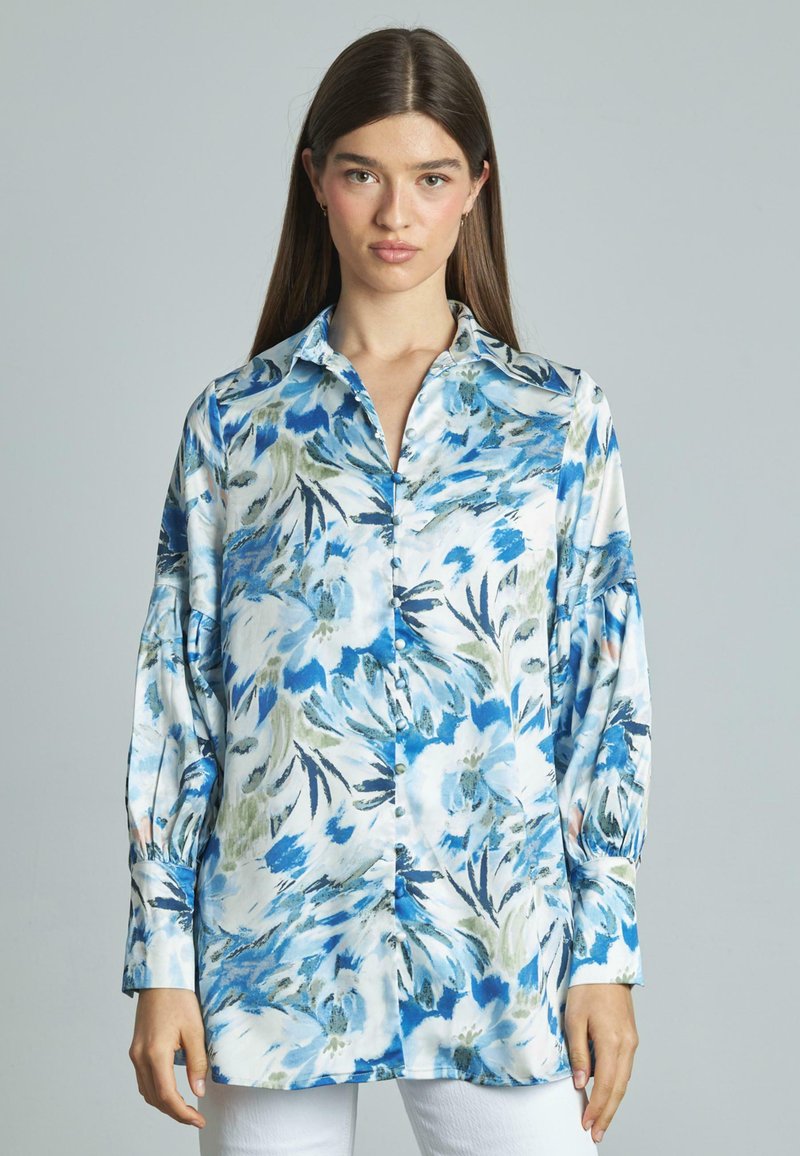 Langsleeve shirt van zijdeachtige stof met een blauw en groen bloemmotief op een witte achtergrond, met een knoopsluiting aan de voorkant en manchet-sleeves.