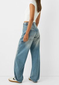 Modré vysoko pasové široké džíny s vybledlým ombré, se zadními kapsami a mírným zúžením na kotnících, stylizované s bílou obuví.