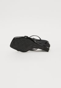 Sandale à talons hauts en cuir verni noir avec une texture lisse, des lanières fines et une semelle en caoutchouc à motifs. Design de talon carré.