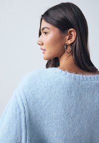 Light blue, soft knit sweater with a loose design, wide neckline, and textured finish. Features dropped shoulders and a relaxed fit.