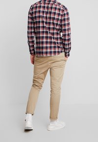 Camicia a quadri nei colori navy, rosso e bianco con colletto a bottone; abbinata a chinos beige e sneakers bianche; design slim-fit.