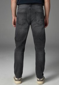 Graue Denim-Jeans im Slim Fit, ausgestattet mit klassischen Gesäßtaschen und einem dezent ausgebleichten Textur, kombiniert mit hellen Schuhen.