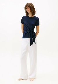 Camiseta de manga corta de color azul marino con detalle de nudo en el costado, combinada con pantalones anchos blancos. Textura de tela suave y corte casual.