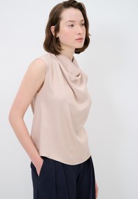 Top senza maniche con scollo a ciambella di un beige chiaro, realizzato in un tessuto morbido. Presenta una silhouette rilassata e un drappeggio sottile all'escollatura.