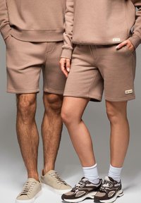 Hnědé bavlněné sportovní šortky a odpovídající oversized trička. Vlastnosti zahrnují žebrované manžety a jemné logo na lemu. Texturovaná tkanina.