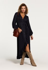 Langes, navy blaues Wickelkleid mit Struktur, V-Ausschnitt, langen �Ärmeln und rüschendem Saum, kombiniert mit beigen Cowboy-Stiefeln und einer braunen Umhängetasche.