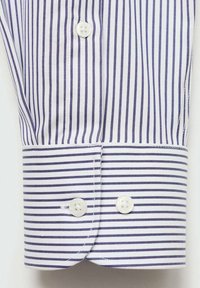 Valkoinen kauluspaita, jossa on kapeita violetinvärisiä raitoja, kaksi valkoista napia ja siisti ompelu. Sujuva kangas rakenne.