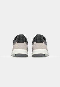 Gray suede sneakers with black accents, white sole, and embossed branding at the heel. Rear view shows minimalistic and modern design.