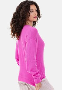 Pull fuchsia en tissu doux avec manches longues, encolure arrondie et poignets et ourlet côtelés. Texture lisse et coupe décontractée.