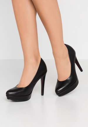 Sorte højhælede pumps i laklæder med rundet tå og platformsål. Har røde accenter på sålerne og et elegant design.