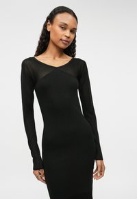 Czarna sukienka z długim rękawem o dopasowanej sylwetce i dekolcie w kształcie litery V. Wykonana z gładkiego, elastycznego materiału z teksturalnym detalem na ramionach.