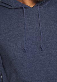 Námořnický modrý mikina s kapucí vyrobená z měkké látky, s šňůrkou na stažení a hladkým povrchem. Jednoduchý design bez vzorů nebo akcentů.