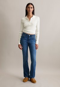 Weißes, geripptes Langarmtop mit Kragen, kombiniert mit blauen, schmalen Jeans und braunen Schuhen. Einfaches Design, Baumwollmaterial und taillierte Form.