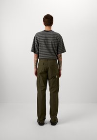 Koszula w paski z krótkim rękawem w odcieniach szarości i granatu, zestawiona z oliwkowozielonymi spodniami typu cargo z wieloma kieszeniami, widocznym przeszyciem i naszywką z logo.