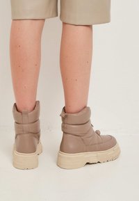 Botines acolchados beige con suela de goma texturizada, que presentan una punta redonda y un diseño de cuello doblado. Parte superior de cuero suave con detalles minimalistas.