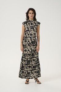 Robe sans manches à motif floral en velours noir et crème. Corsage ajusté avec une jupe maxi évasée. Portée avec des sandales noires à lanières.