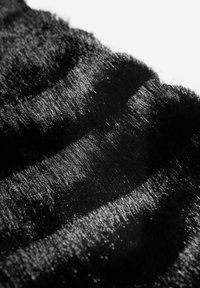 Melnas vilnas audums ar mīkstu, spīdīgu tekstūru, kas rāda smalkus gaismas atspīdumus un viļņainus rakstus tās virsmā.