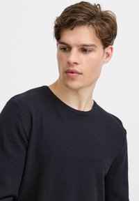 Pulover tricotat texturat de un albastru închis, cu decolteu la baza gâtului și mâneci lungi, având un model subtil în formă de vafe pe întreaga țesătură.