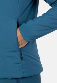 Blå isoleret jakke med en sidelomme og en lynlåsdetalje. Glat, blød tekstur med en tætsiddende design for komfort og varme.