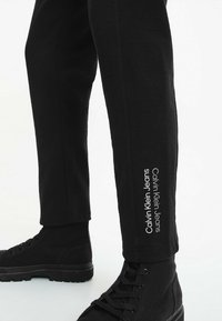 I pantaloni jogger in cotone nero presentano una vestibilità aderente con orlo a costine e il logo bianco "Calvin Klein Jeans" stampato lungo un lato.