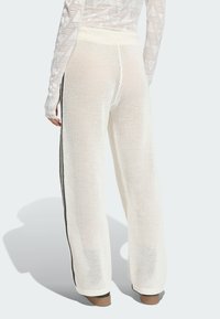 Osoba oblečená v bielych širokých sieťovaných nohaviciach s čiernymi bočnými pruhmi a v bielom sieťovanom dlhom rukáve, zobrazená zozadu.