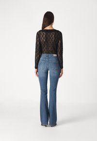 Top de encaje negro de manga larga combinado con jeans acampanados de color azul claro. Los jeans tienen bolsillos traseros y una textura ligeramente deslavada.