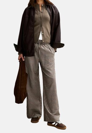 Bruine leren jas, grijze gebreide cardigan, losse bruine en witte geruite broek en bruine sneakers met witte strepen en mintkleurige accenten.