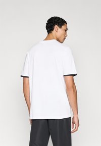 Λευκό μπλουζάκι με κοντά μανίκια, γκρι αντίθετη επένδυση στα μανσέτα, στρογγυλεμένος λαιμός και άνετη εφαρμογή, φορεμένο με σκούρο σορτς.