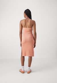 Robe halter rose pâle à côtes avec un corsage ajusté, ourlet à hauteur du genou et fente latérale. Associée à des chaussures rayées roses et des chaussettes blanches.