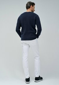 Maglione in maglia testurizzata blu navy, pantaloni slim-fit bianchi e sneakers nere. Vista da dietro, che mostra il design aderente e linee pulite.