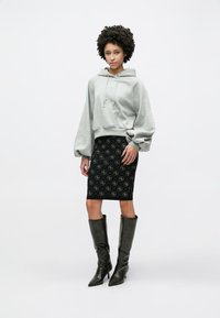 Γκρι φούτερ με κορδόνια, μαύρη φούστα-μολύβι με σχέδιο και μαύρες μπότες μέχρι το γόνατο. Το μοντέλο στέκεται με τα χέρια μπροστά, ουδέτερο φόντο.
