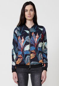 Giacca bomber con zip frontale, base nera e stampa floreale vivace in tonalità di rosso, blu e verde, con polsini e orlo a coste.
