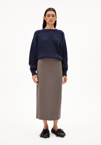Pull en maille côtelée bleu marine, jupe midi beige, mocassins à franges noirs avec accents dorés. Design simple et structuré, motifs minimalistes.