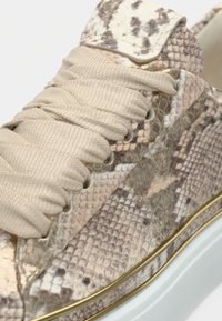 Αθλητικό παπούτσι με επάνω μέρος σε μπεζ σχεδιασμό φιδιού, χοντρές μπεζ κορδόνια και λευκή σόλα με λεπτή χρυσή ρίγα.