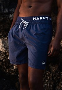 Marineblauwe zwembroek met elastische tailleband, voorzien van "HAPPY" in het wit, trekkoordsluiting en een klein logodetail op het been.