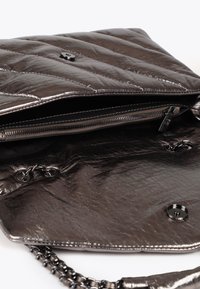 Detailní záběr na kovovou tmavě šedou kabelku, který zobrazuje její prošívanou texturu, řetízkový popruh a otevřenou kapsu se zipem vyloženou látkou.