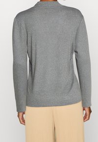 Grå stickad tröja med långa ärmar, rund hals och en texturerad yta. Baksidan har en enkel design utan utsmyckningar.