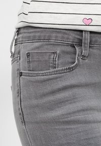 Jeans de mezclilla gris con un corte ajustado, que presentan un pequeño bolsillo frontal, costuras sutiles y una textura ligeramente descolorida. Acabados con un diseño de corazón en la camiseta de arriba.