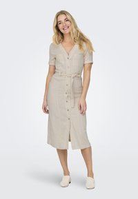 Beige linnedrakt med korte ermer, knapplukking foran, to brystlommer og en knyttet midjebelte, med en rett, midi lengde.
