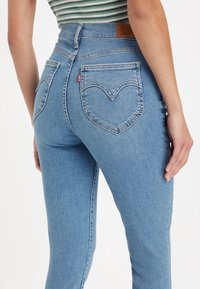 Jeans de denim azul claro con cintura alta, corte ajustado y bolsillos traseros en forma de corazón. Tejido texturizado con detalles de costura sutiles.