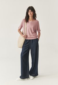 Lichtroze korte mouwen top, losse donkere denim wijde broek, en witte sneakers. Beigekleurige schoudertas maakt de outfit compleet.