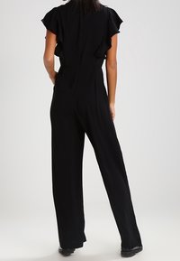 Mono negro con mangas acampanadas, cintura ajustada y diseño de pierna ancha. Tela suave, detalles mínimos y una vista trasera limpia.