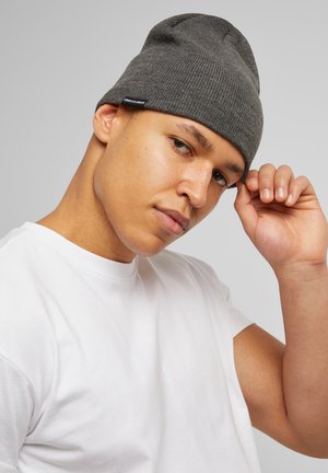 Grey knit beanie with ribbed texture, fitted design, and a small logo tag. Worn by a person in a white t-shirt.