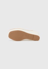 Sandale plateforme blanche avec un dessus texturé et une semelle en caoutchouc marron. Présente un design léger et une marque de la marque discrète sur la semelle.
