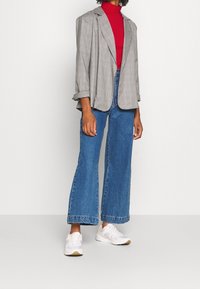 Gray plaid blazer with a relaxed fit, worn over a red turtleneck, paired with high-waisted blue wide-leg jeans and white sneakers.