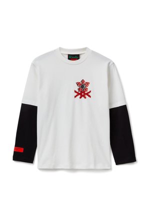 Weißes Langarmshirt mit schwarzen Ärmeln, pixelgrafischem roten und schwarzen Blumenmotiv auf der Brust und rotem Etikett am linken Ärmelsaum.